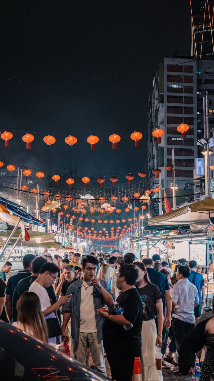 Vibrant street scene of a crowded night market with hanging red lanterns.