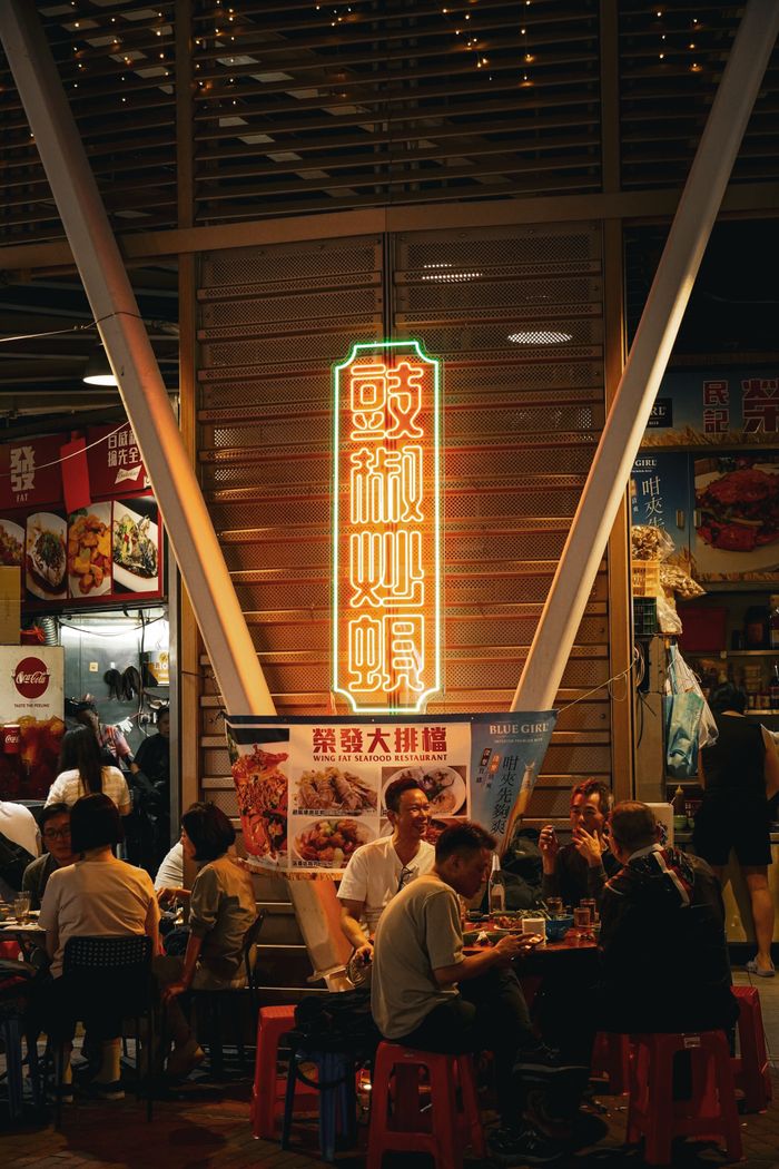 Capture the lively atmosphere of a Hong Kong street market at night with neon signs and dining locals.